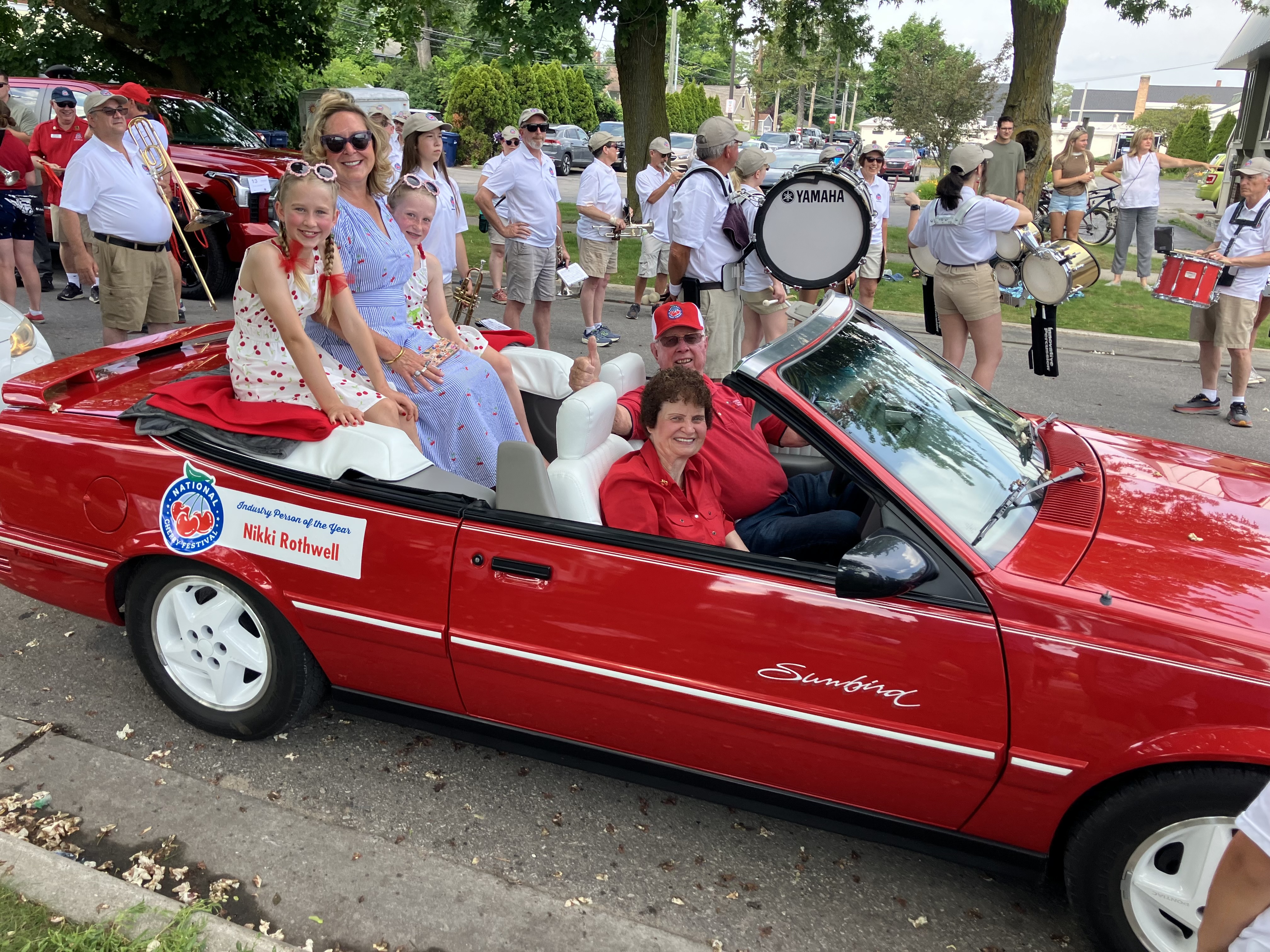 Nikki Rothwell rides in the backseat of a red convertible during a parade.